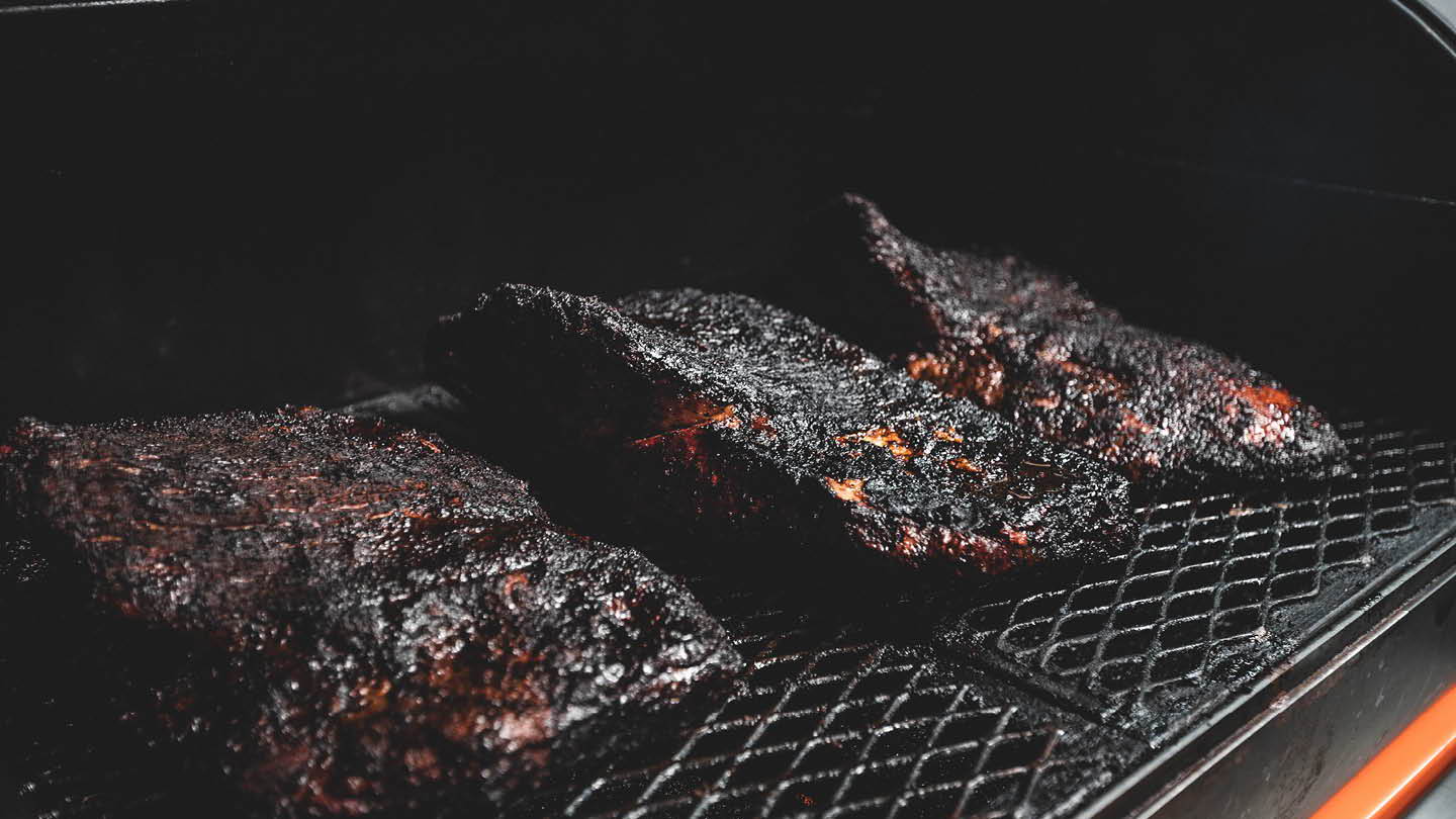 Three smoked meats on a grill, showcasing a dark, charred exterior.
