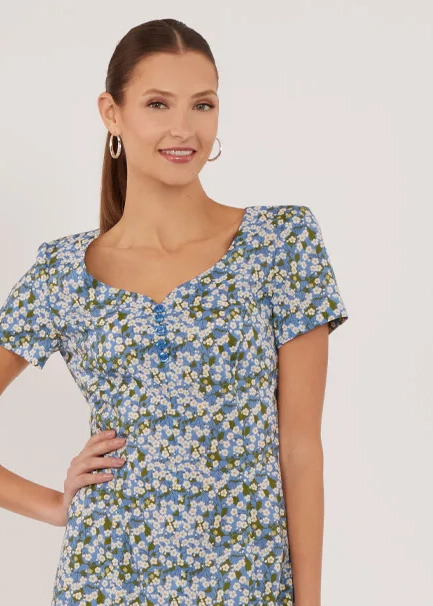 Woman smiling in a floral dress with short sleeves.