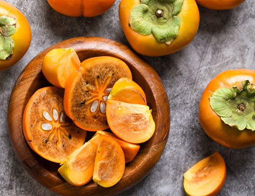 Sliced persimmons in a wooden bowl on a textured surface.