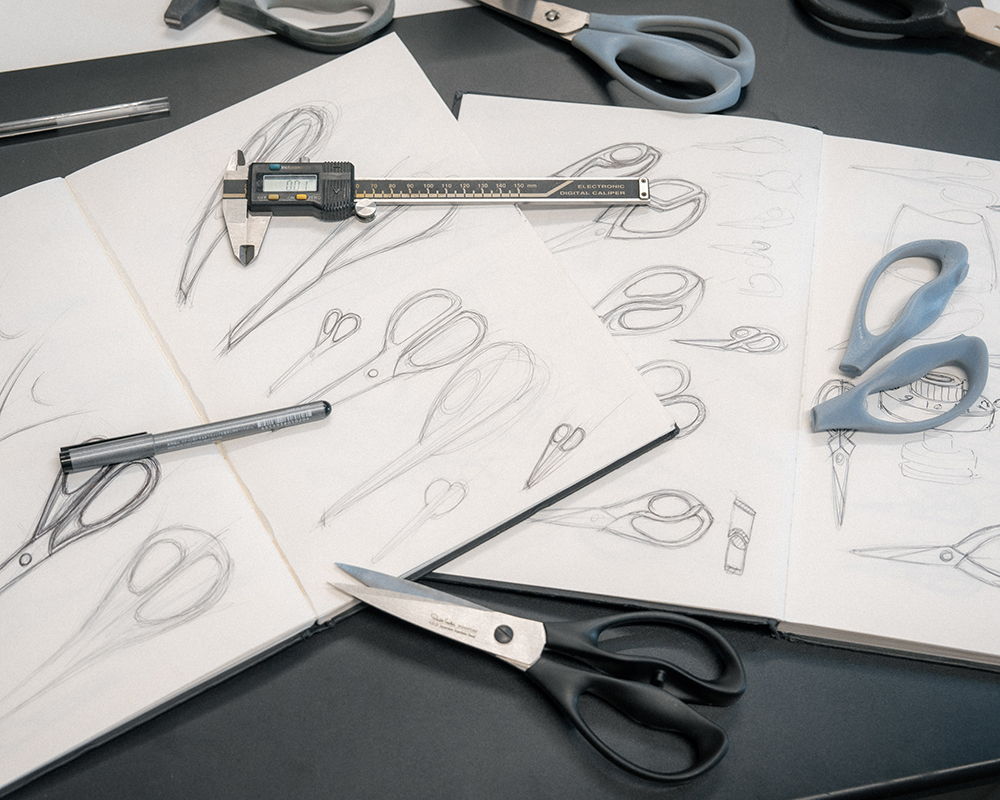 Signature Scissors and drawing tools scattered on sketch papers.