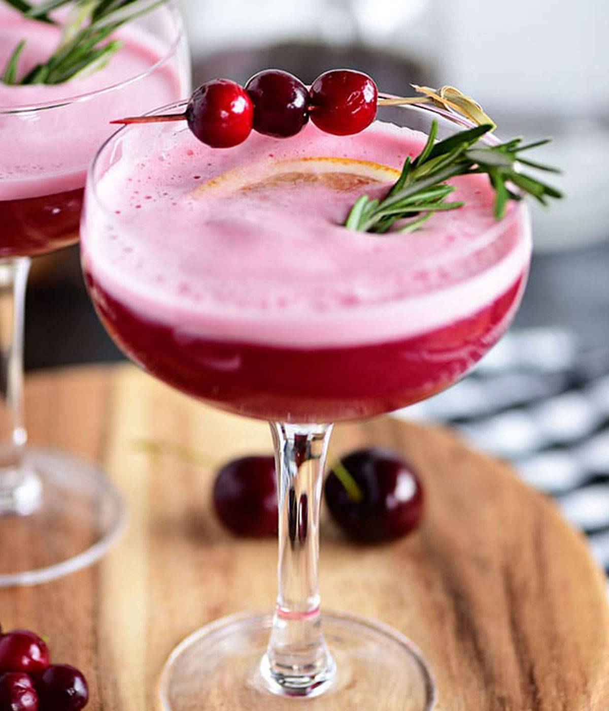 A dark pink cocktail with berries and rosemary on top of drink. 