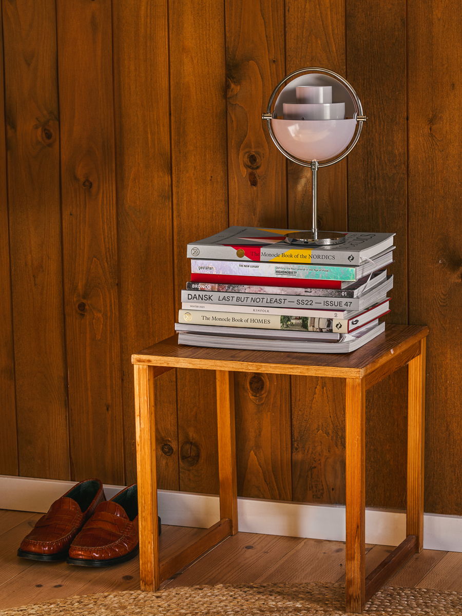 A wooden side table with stacked books and a lamp, near shoes.