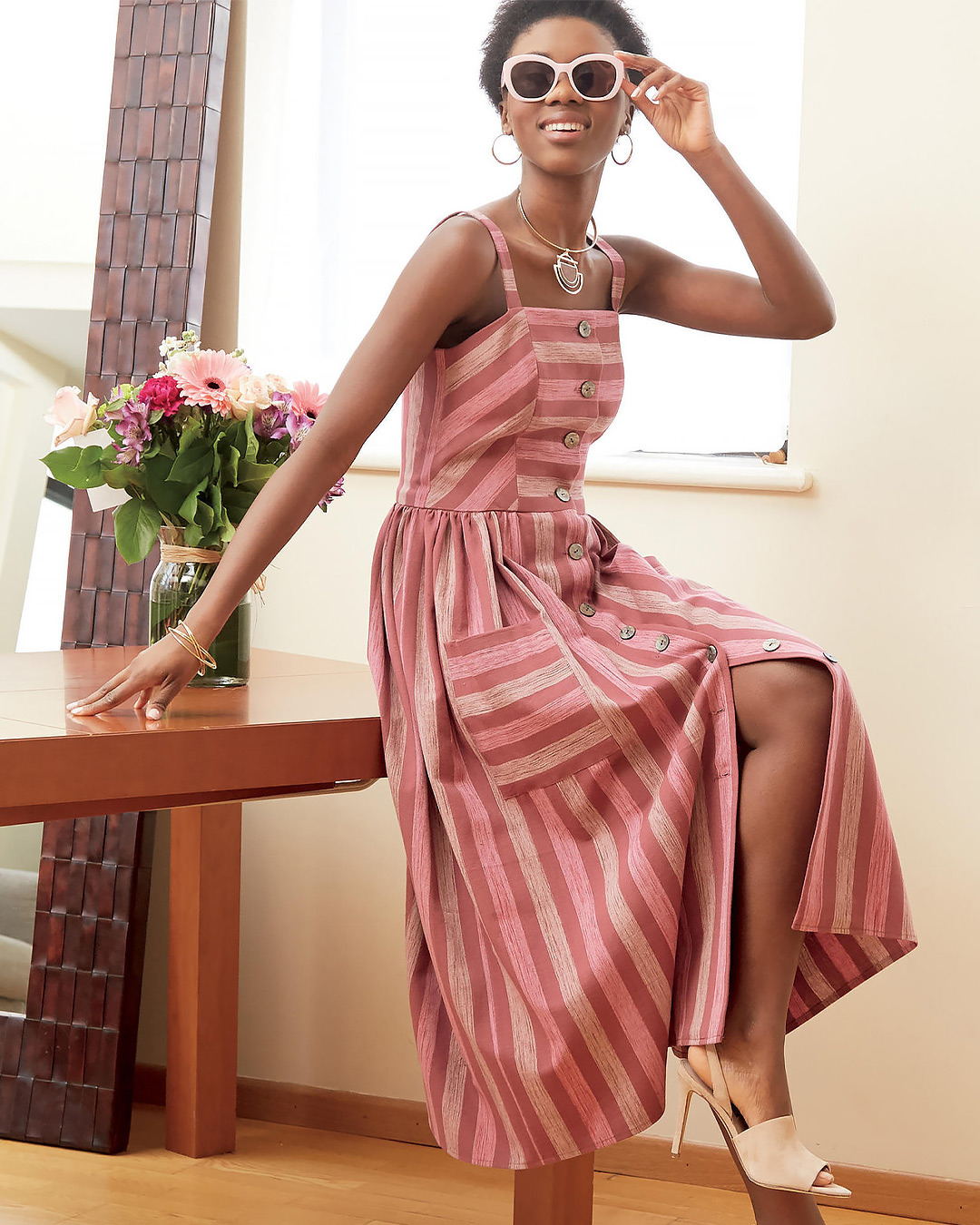 Woman in a striped dress posing with sunglasses and flowers nearby.