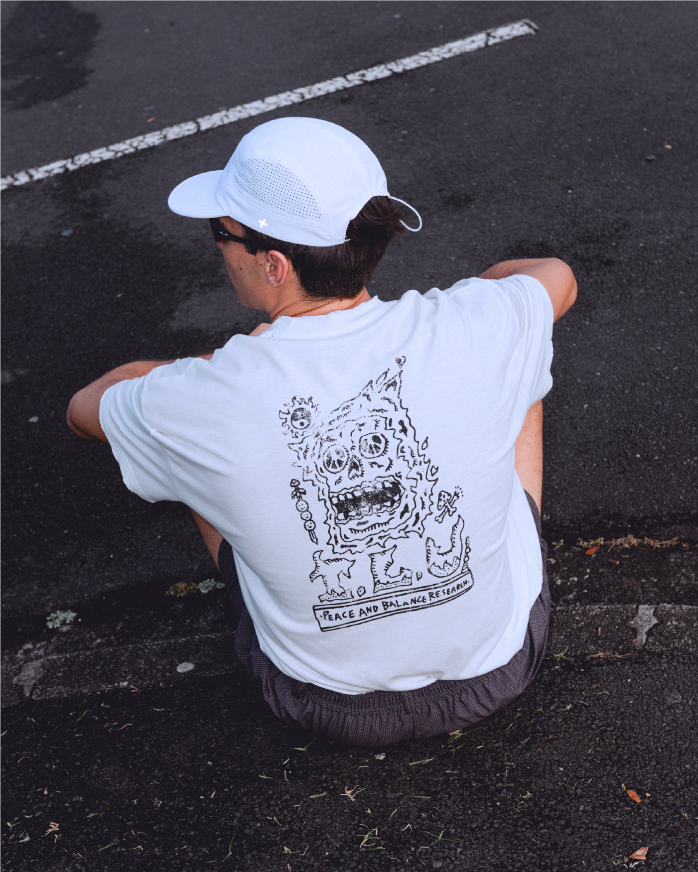 Person sitting on pavement wearing a white shirt with a graphic design.