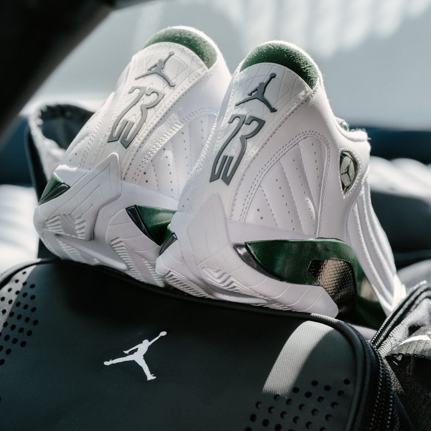 White and green Air Jordan sneakers on top of a black bag.