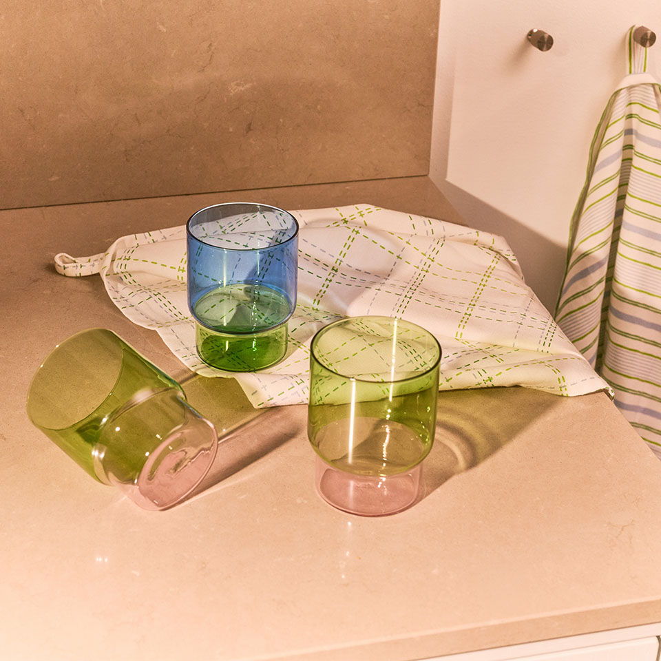 Three colorful glasses and a dish towel on a countertop.
