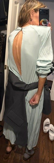 Woman in a light blue dress with an open back, taking a mirror selfie.
