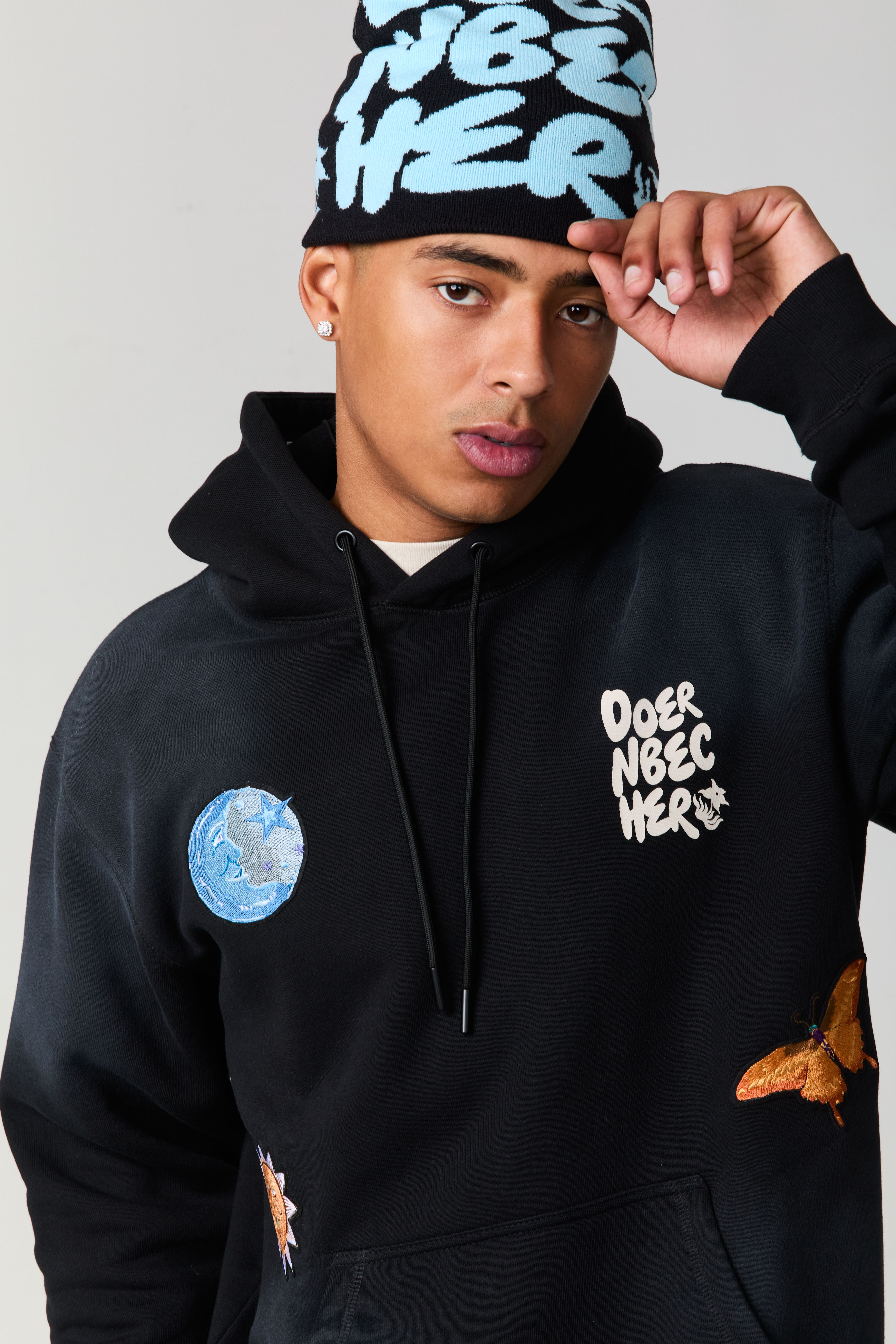 Person wearing a black hoodie and blue beanie, posing confidently.