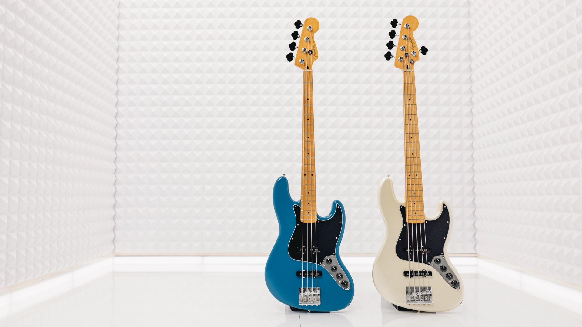 Two Fender Player II Modified Jazz Basses, one blue and one white, on a white textured background.