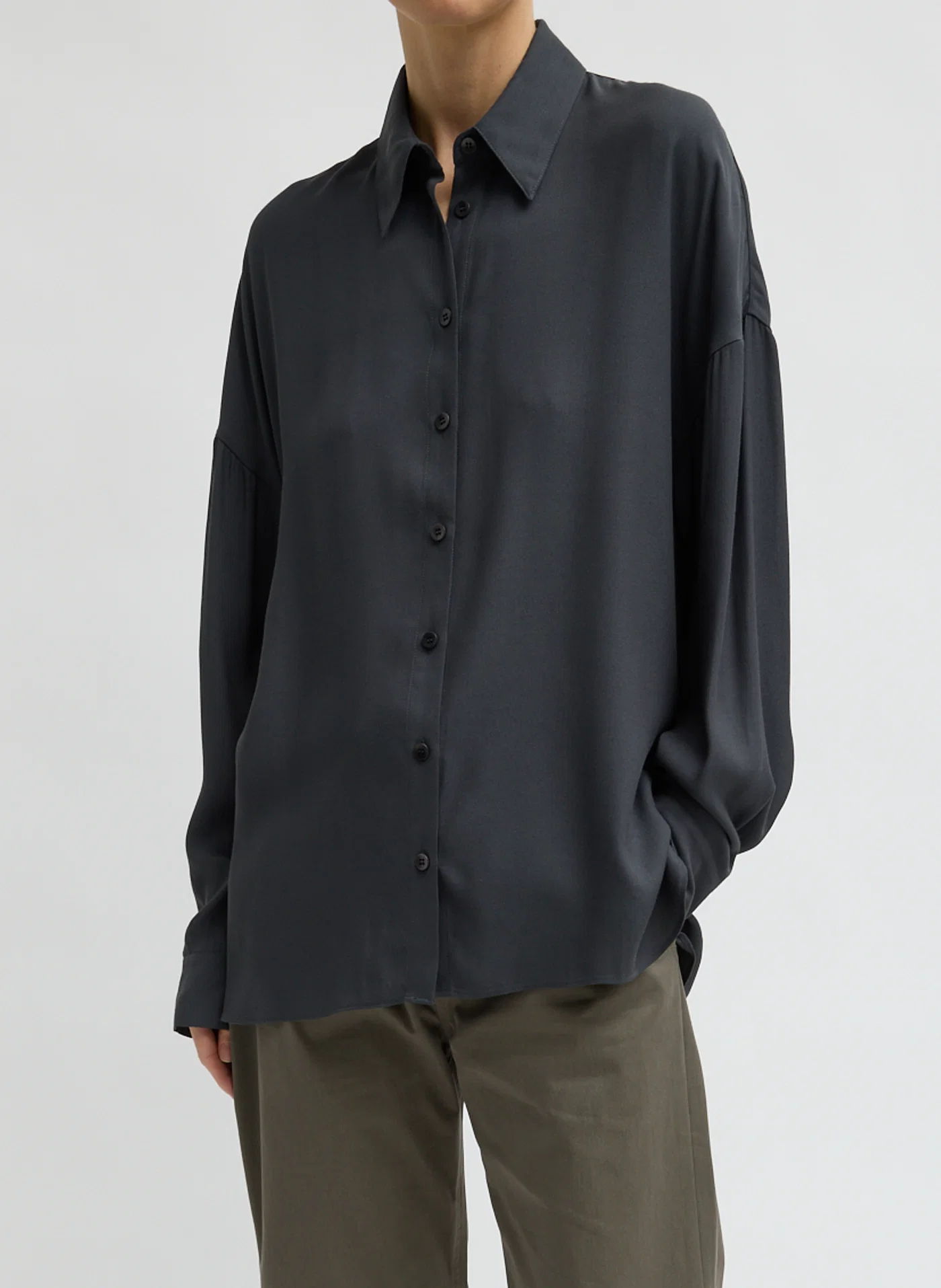 Person wearing a dark button-up shirt and light pants, standing against a neutral background.