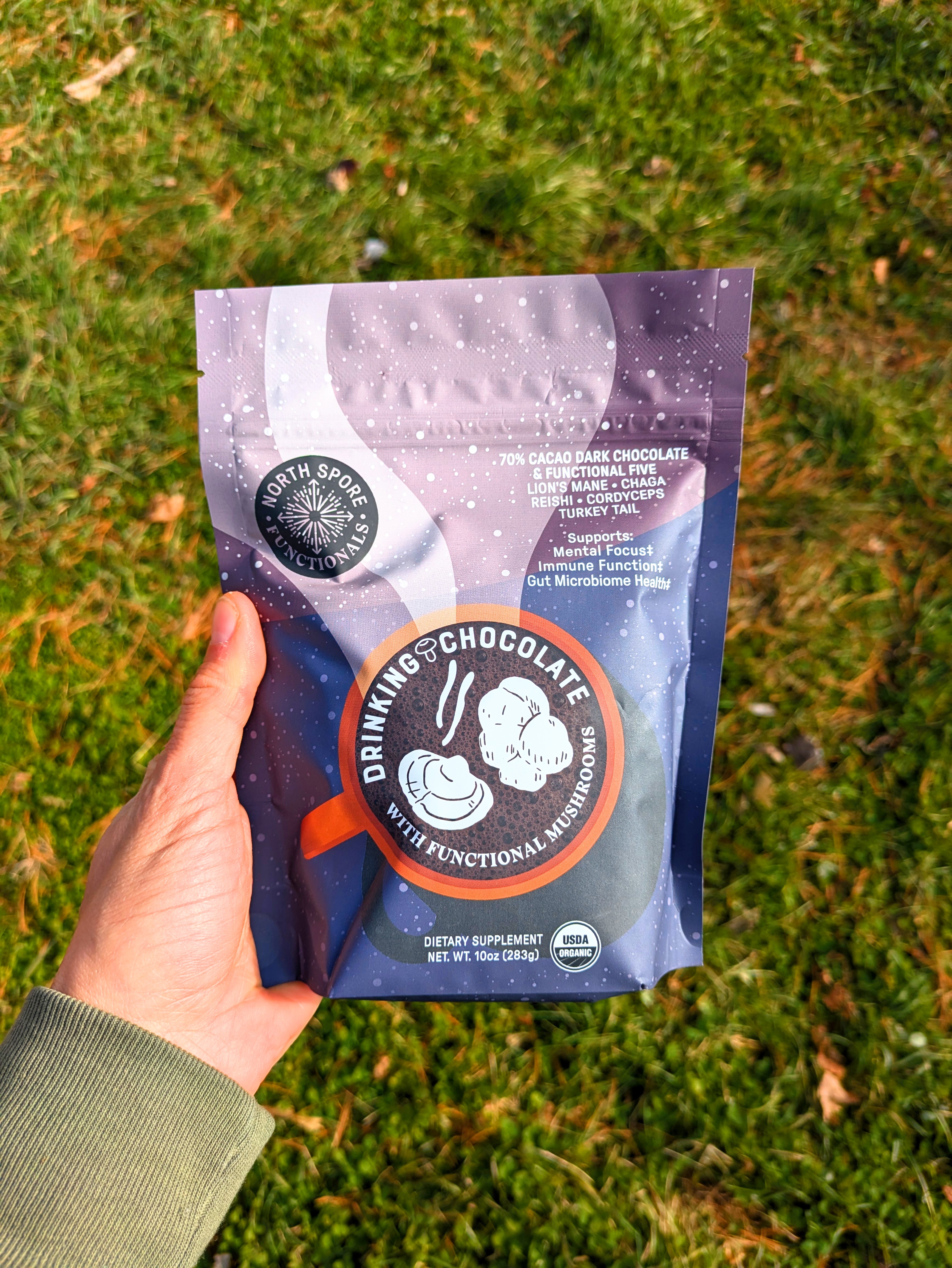Hand holding a bag of drinking chocolate on grass background.