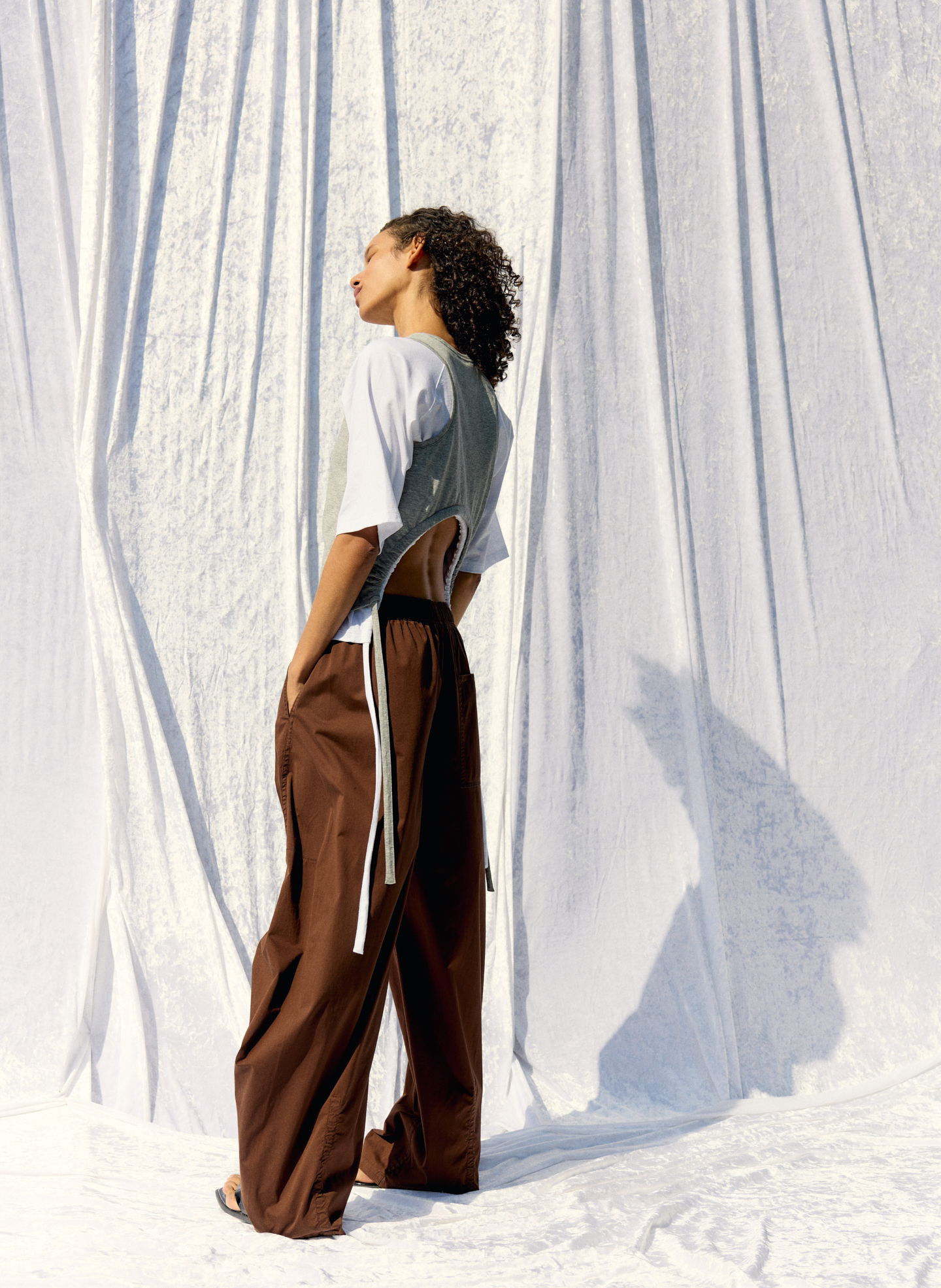 Person in stylish outfit stands against a white backdrop, showcasing fashion.