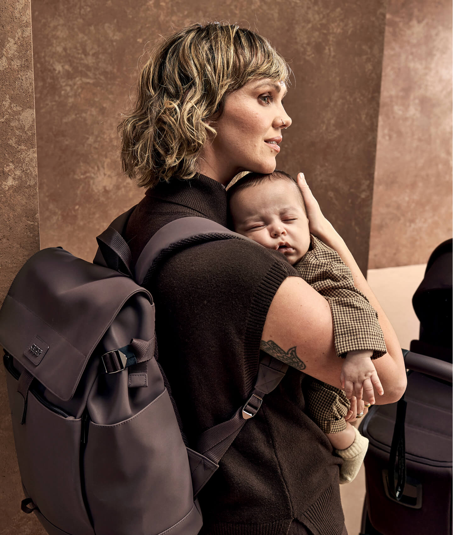 Woman holding a sleeping baby while wearing a backpack.