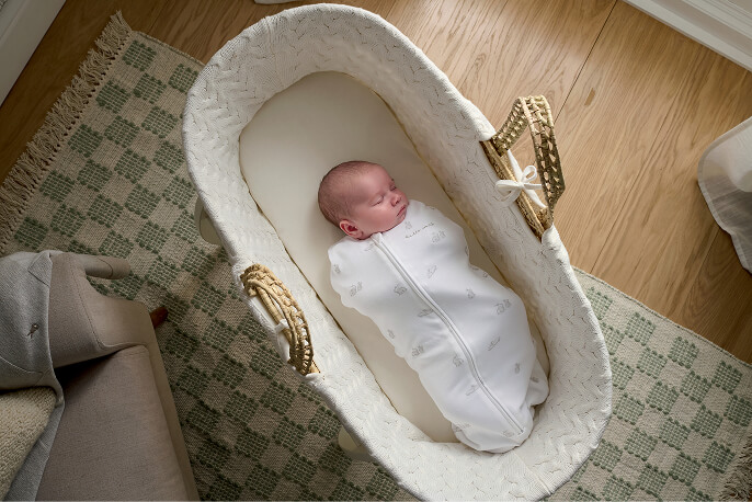 A swaddled baby lying in a basket on a wooden floor.