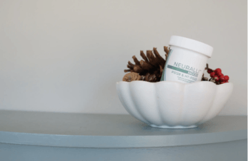 A white bowl with pinecones and a jar on a shelf.