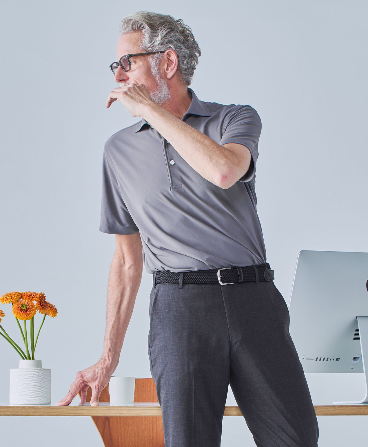 A man in a gray polo shirt stands by a desk with flowers.