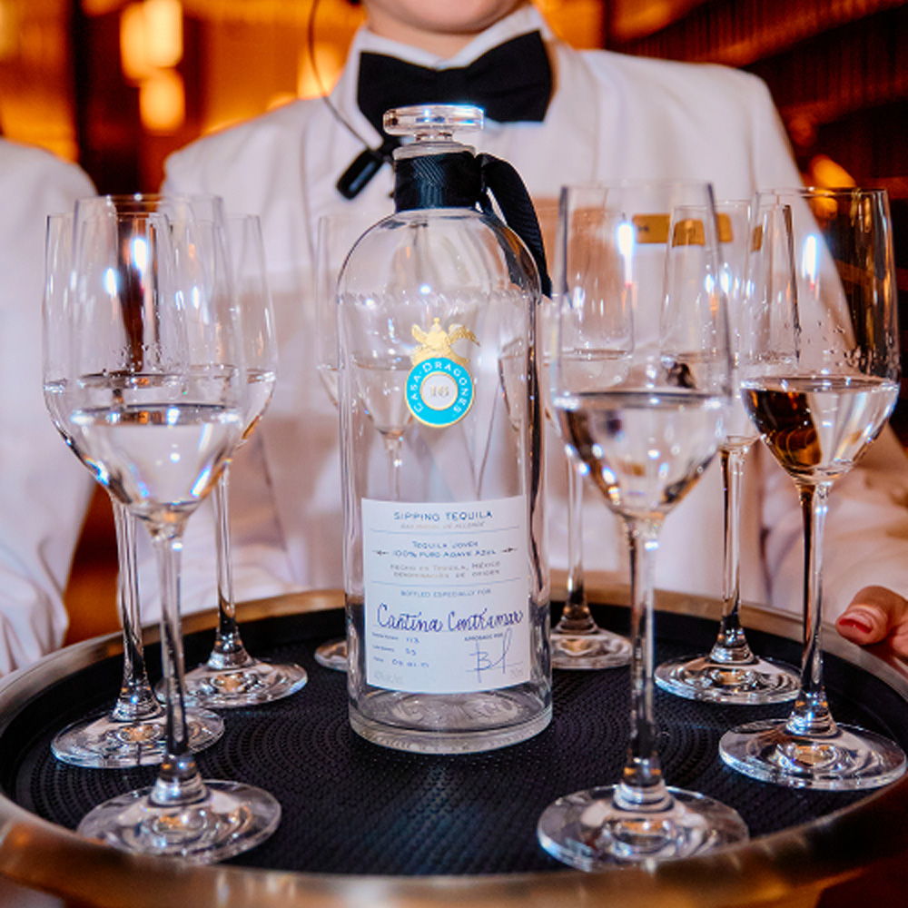 A waiter holding a tray with glasses and a bottle of water.