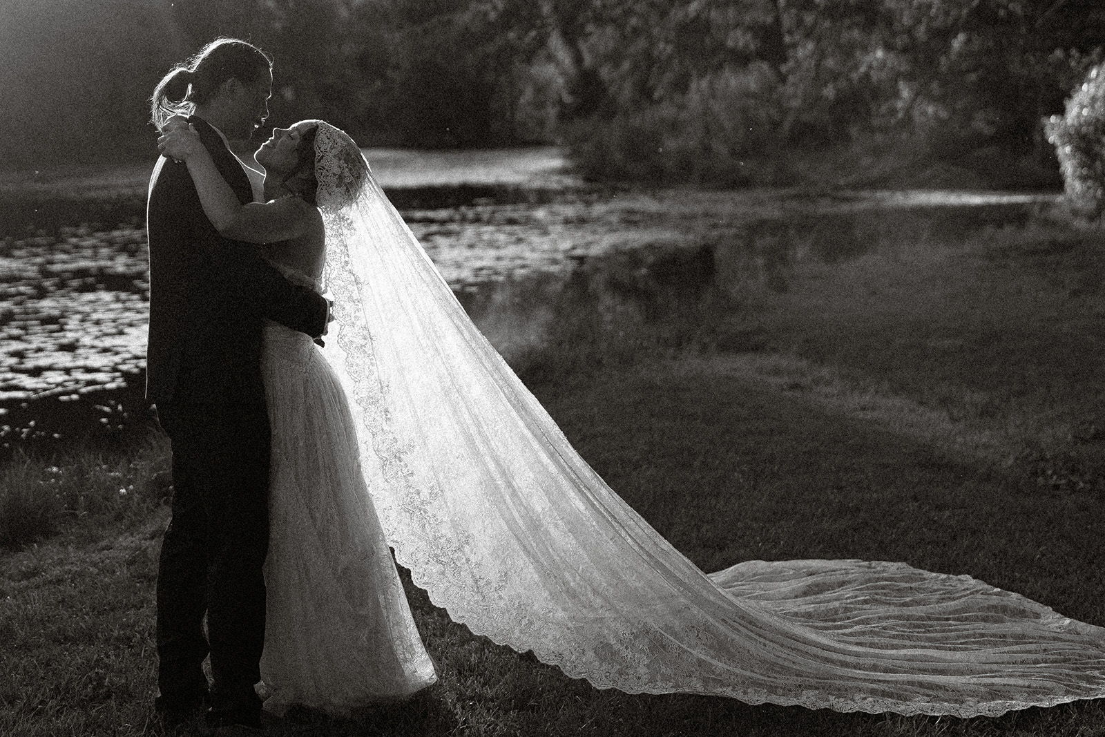 Couple embracing in a romantic outdoor setting, with a flowing wedding veil.