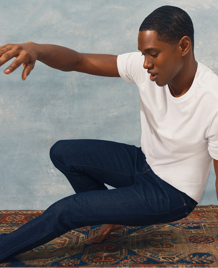 A man in a white shirt poses dynamically on a patterned rug.