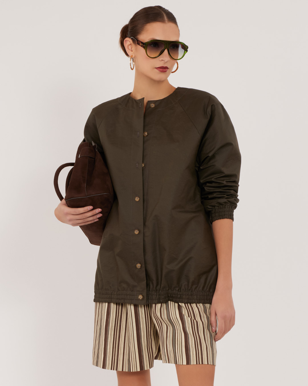 Woman wearing a brown jacket and striped shorts, holding a handbag.