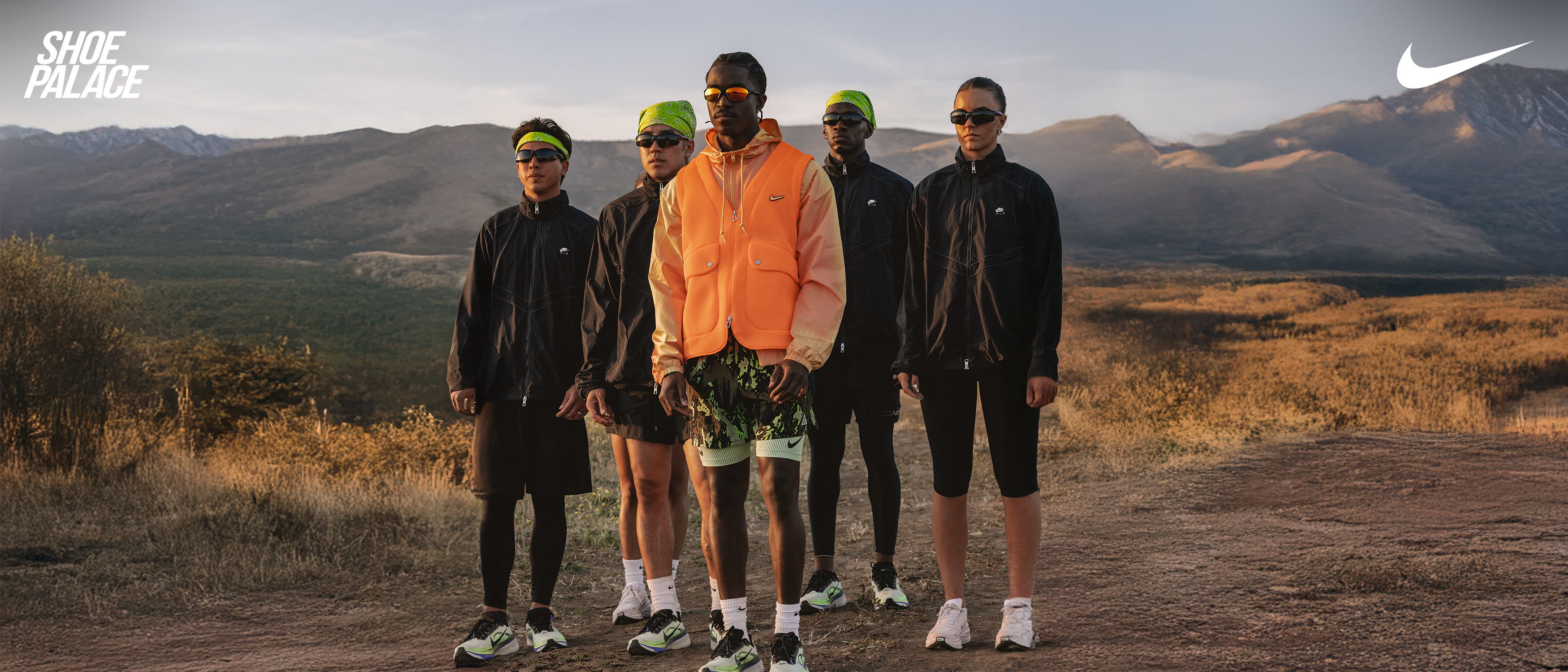 Five individuals standing on a trail in athletic wear against a mountain backdrop.
