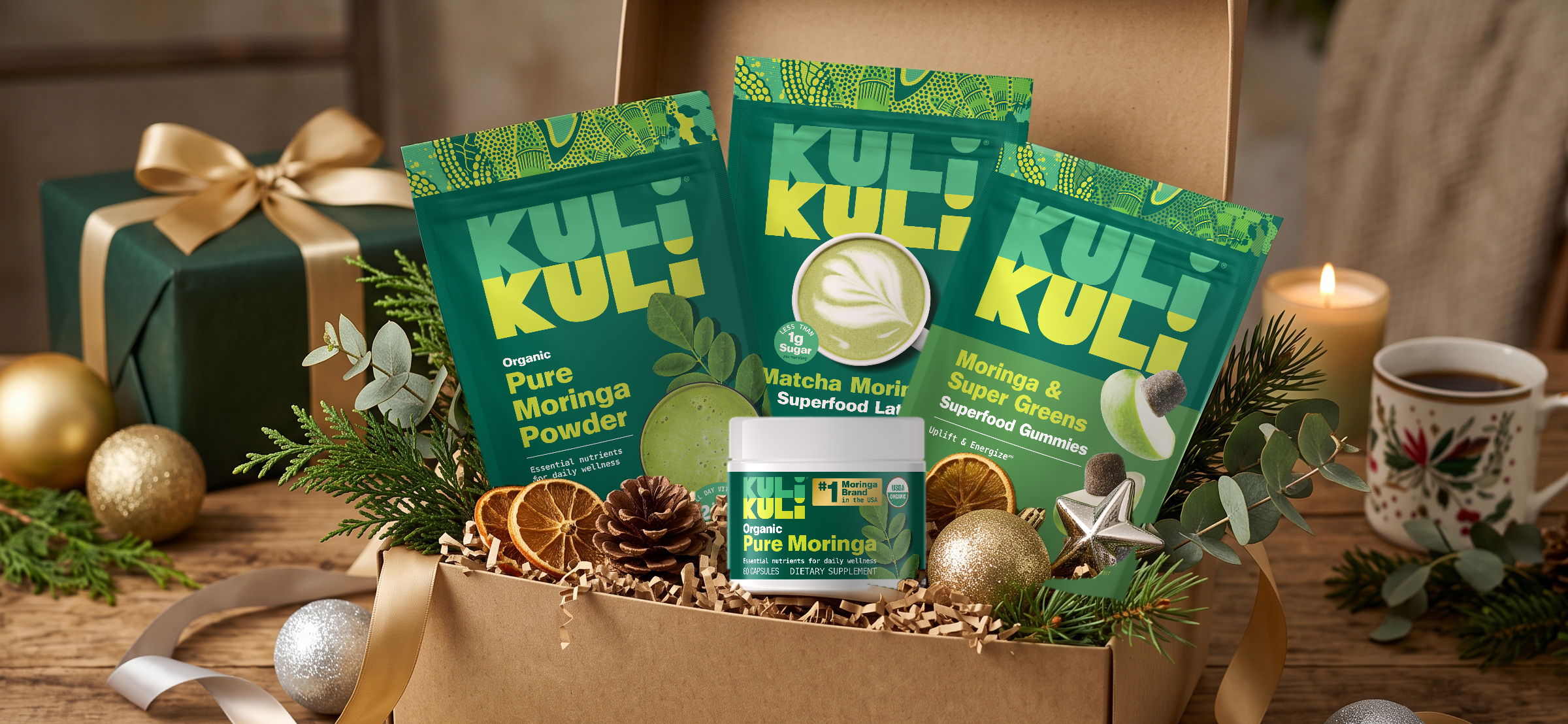 Kuli Kuli moringa powder, matcha latte, greens gummies and capsules in a holiday gift box with evergreens and ornaments.