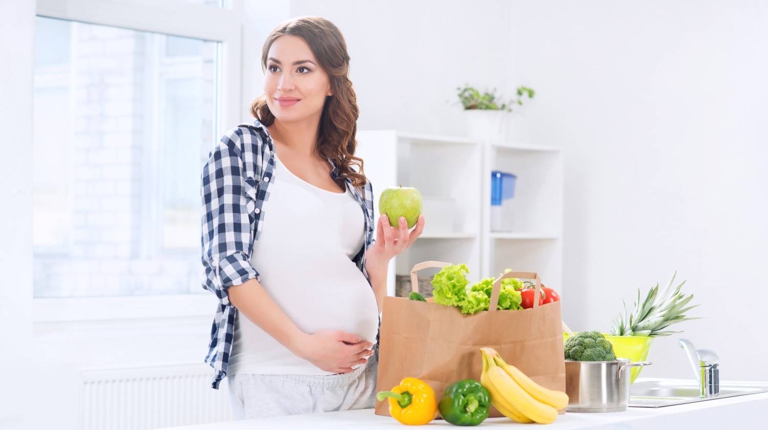 Beautiful pregnant woman in the kitchen with shopping bag and apple | Vegan Pregnancy Diet: Top 8 Foods That Are Good For You And Your Baby | green leafy vegetables | Featured