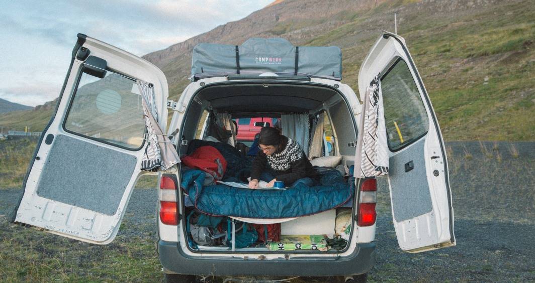A person chilling on top of a Rumpl blanket spread out in the back of a camper van