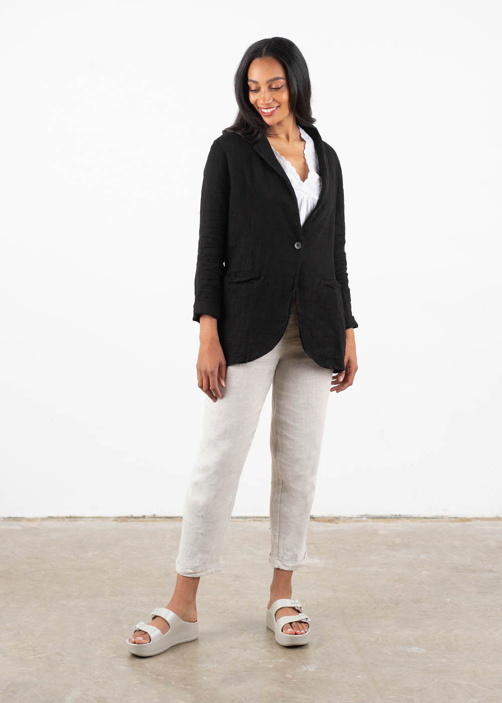 A model wearing a black linen jacket over a white top, taupe linen trousers and off white chunky platform slides
