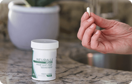 Person holding a pill near a container on a countertop.