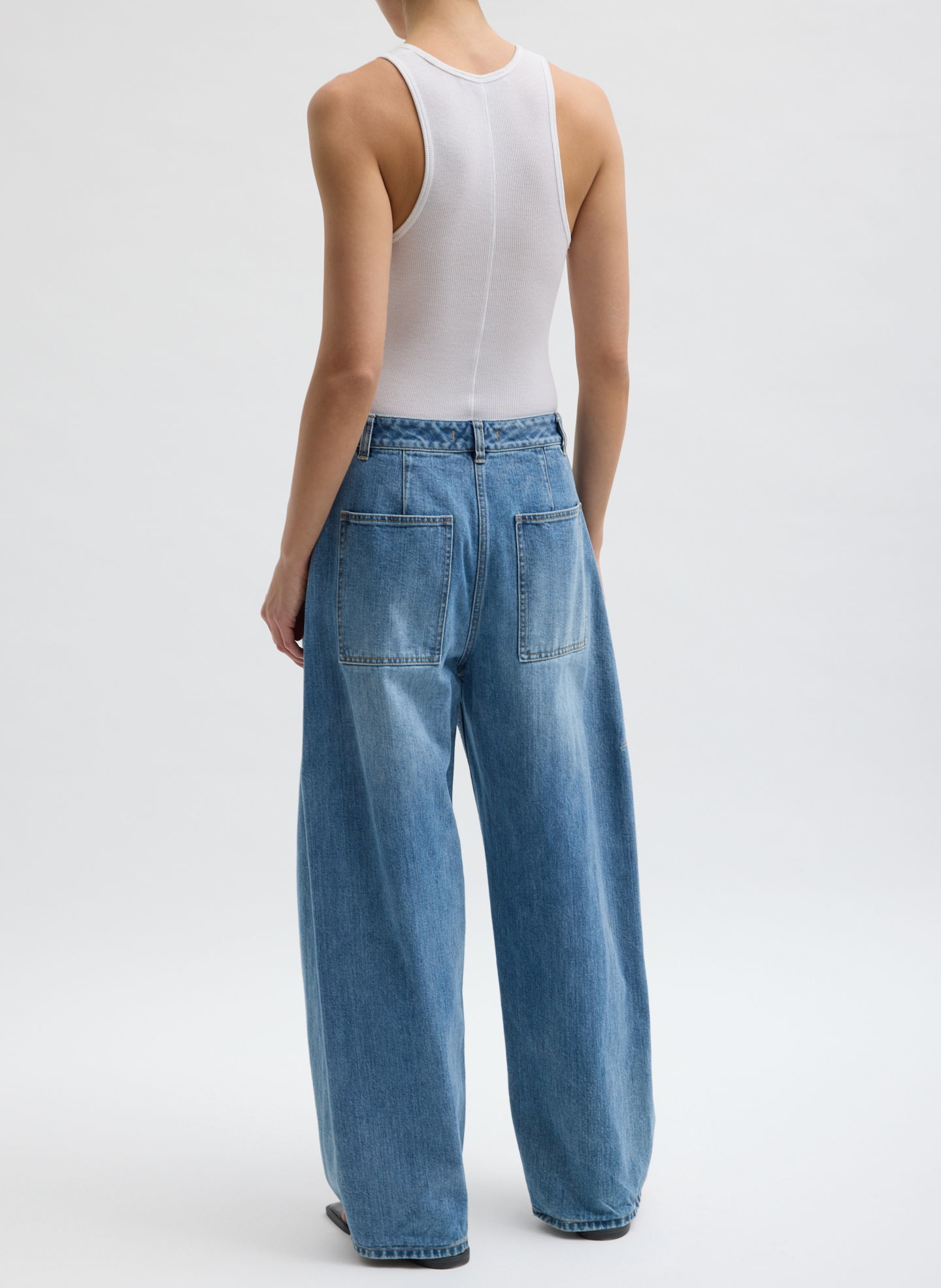 Person wearing a white tank top and baggy blue jeans, viewed from behind.