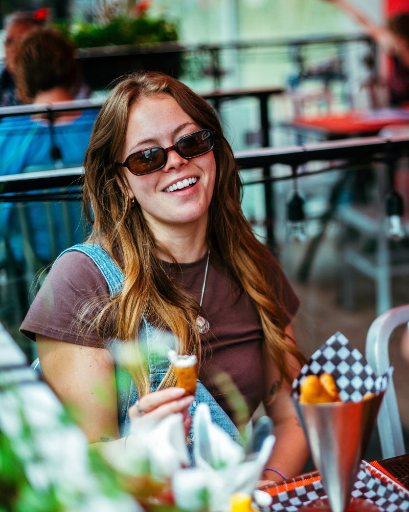 Smiling woman in sunglasses holding a cone, sitting at a café.
