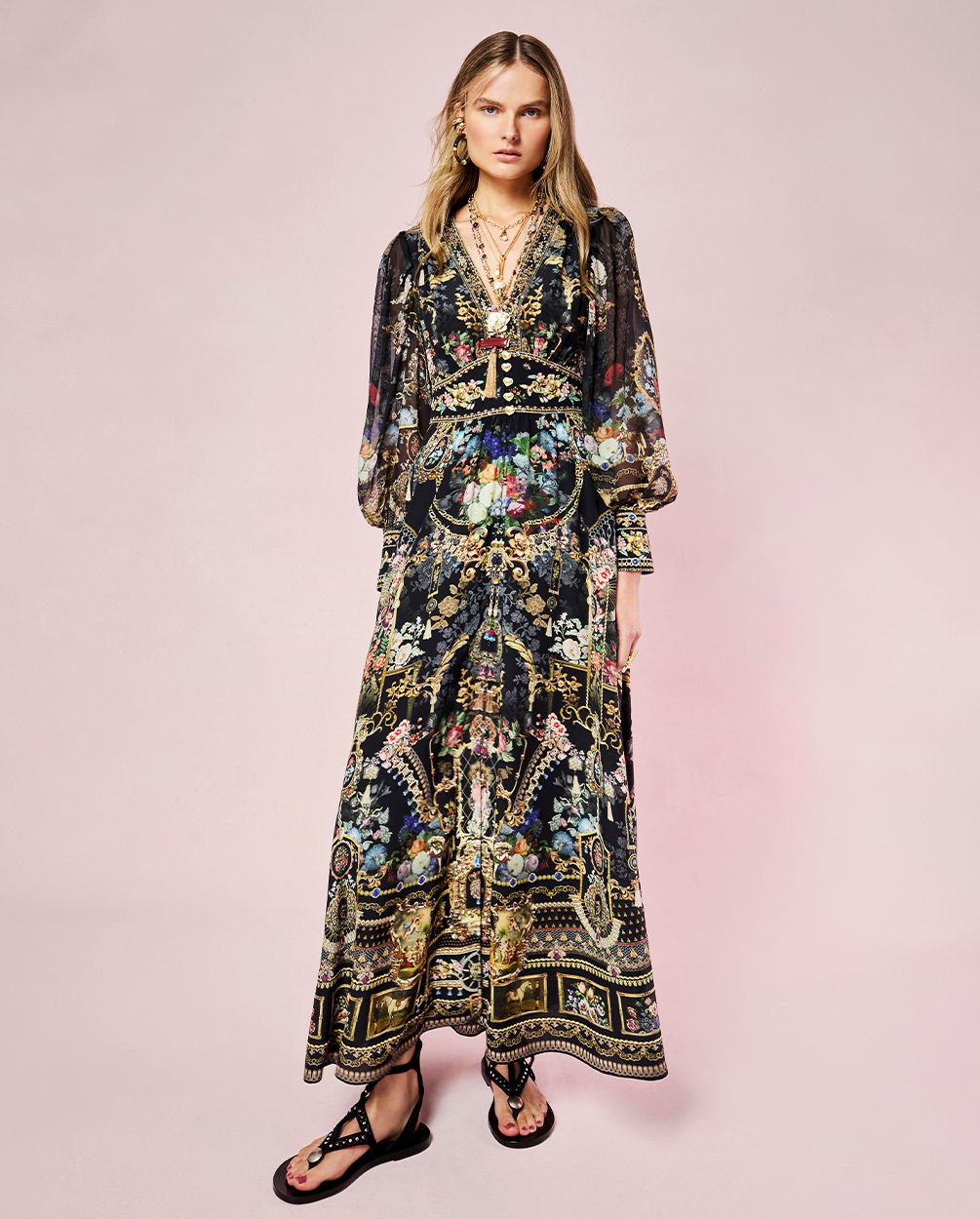 Model wearing a colorful, patterned maxi dress against a pink background.