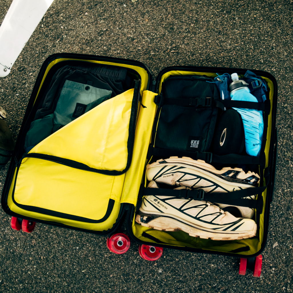 Open suitcase with clothes and shoes on a pavement.