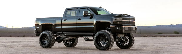Side profile of Elias's black lifted 2015 Chevrolet Silverado 2500HD on large black wheels in the desert, Conductor's Special 544 Nightmare Edition install photo 1