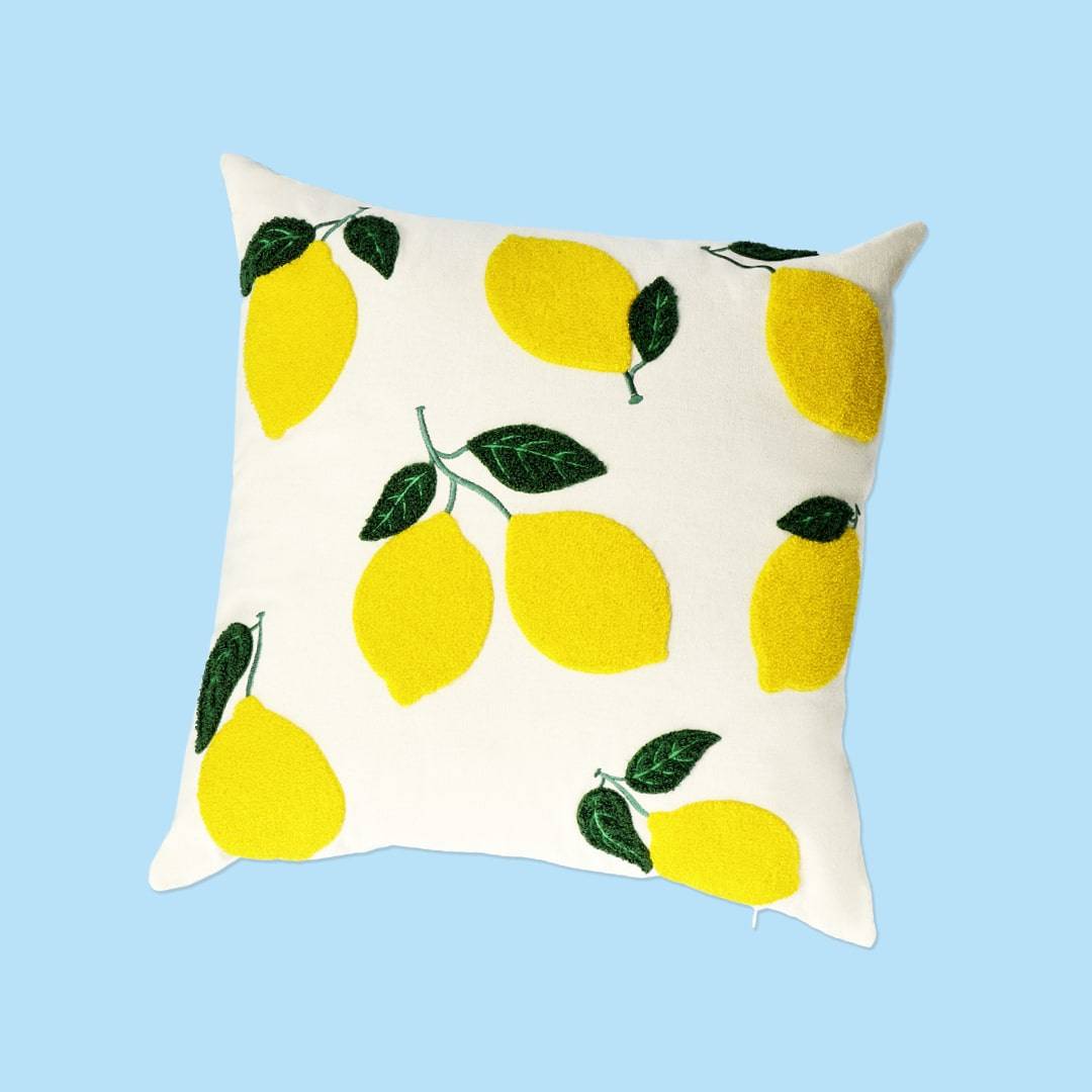 A white decorative pillow adorned with bright yellow lemon prints and green leaves, set against a light blue background.