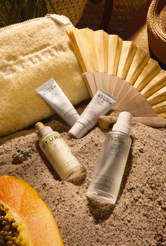 Skincare products arranged on sand with accessories like a fan and pouch.