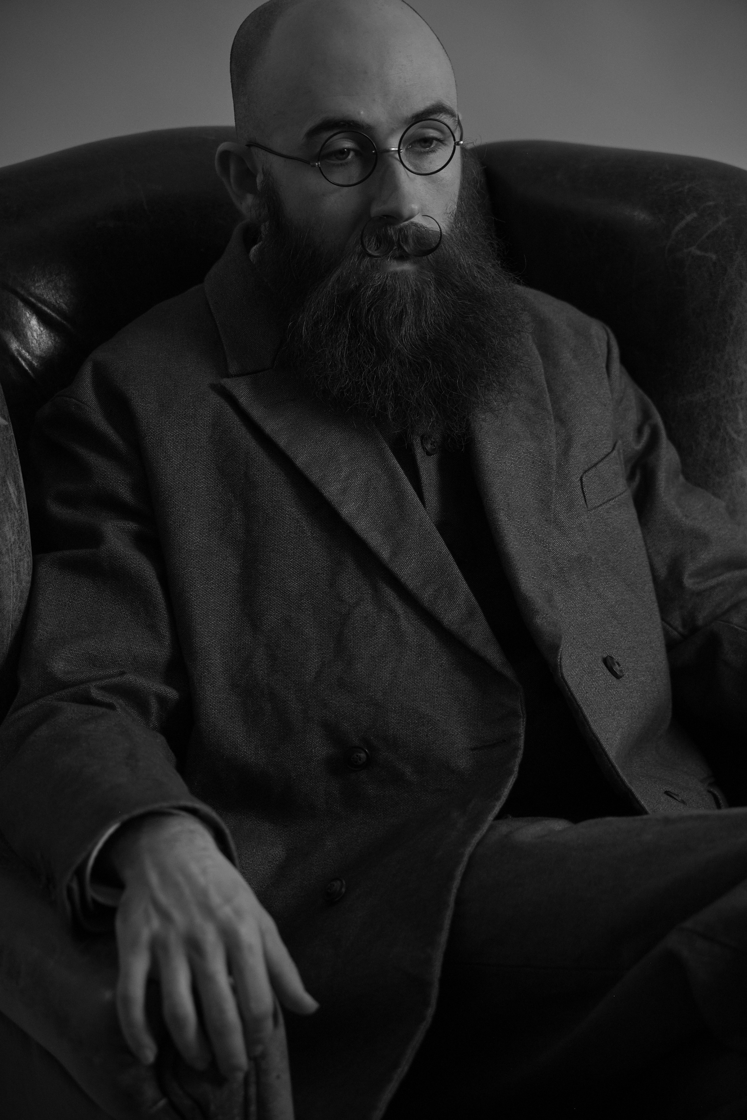 A man with glasses and a beard sitting on a leather couch.