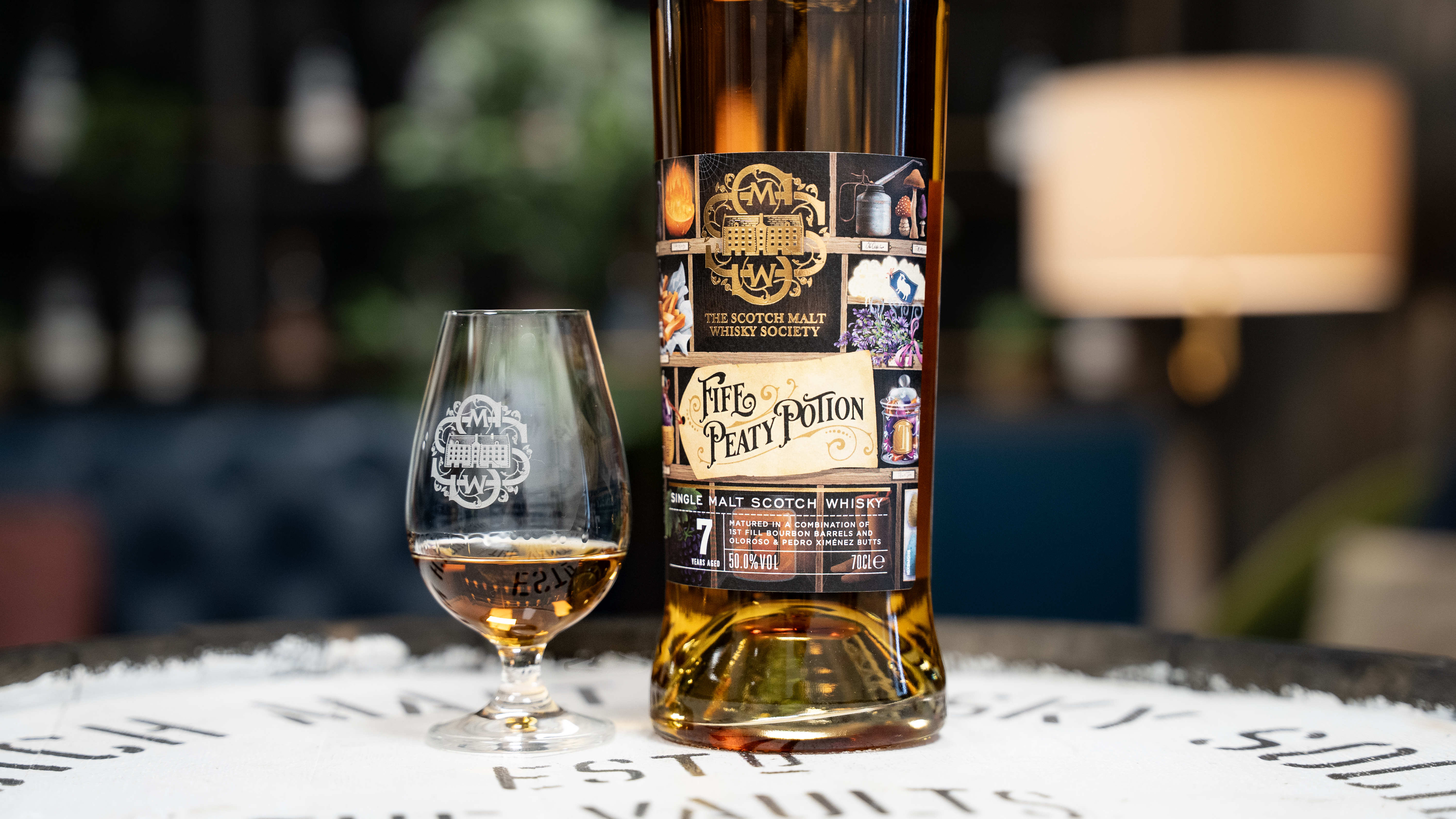 A bottle of whiskey with a glass on a table.