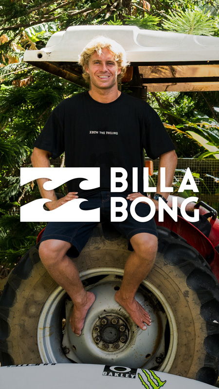 Man sitting on a tractor, smiling, with greenery in the background.