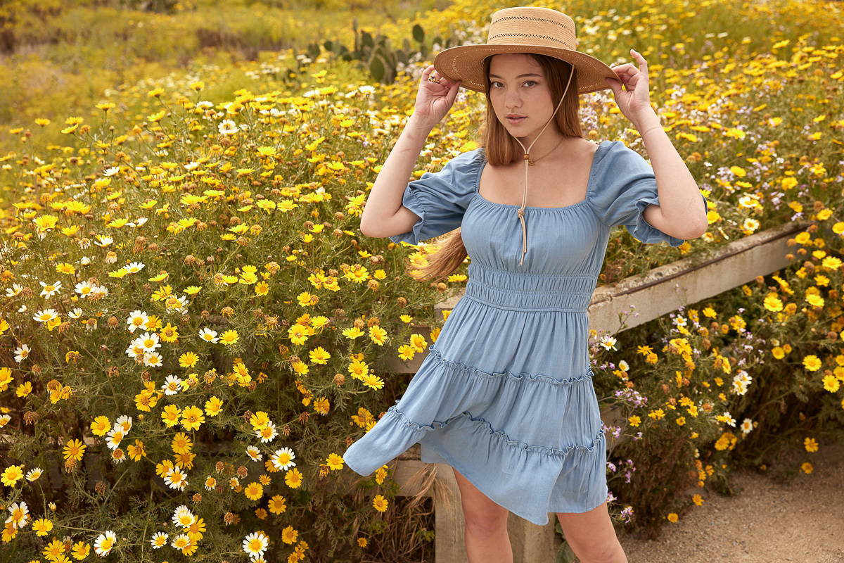 Trixxi sun-kissed summer lookbook, girl with blue tiered mini dress in sun hat in field of yellow flowers. 