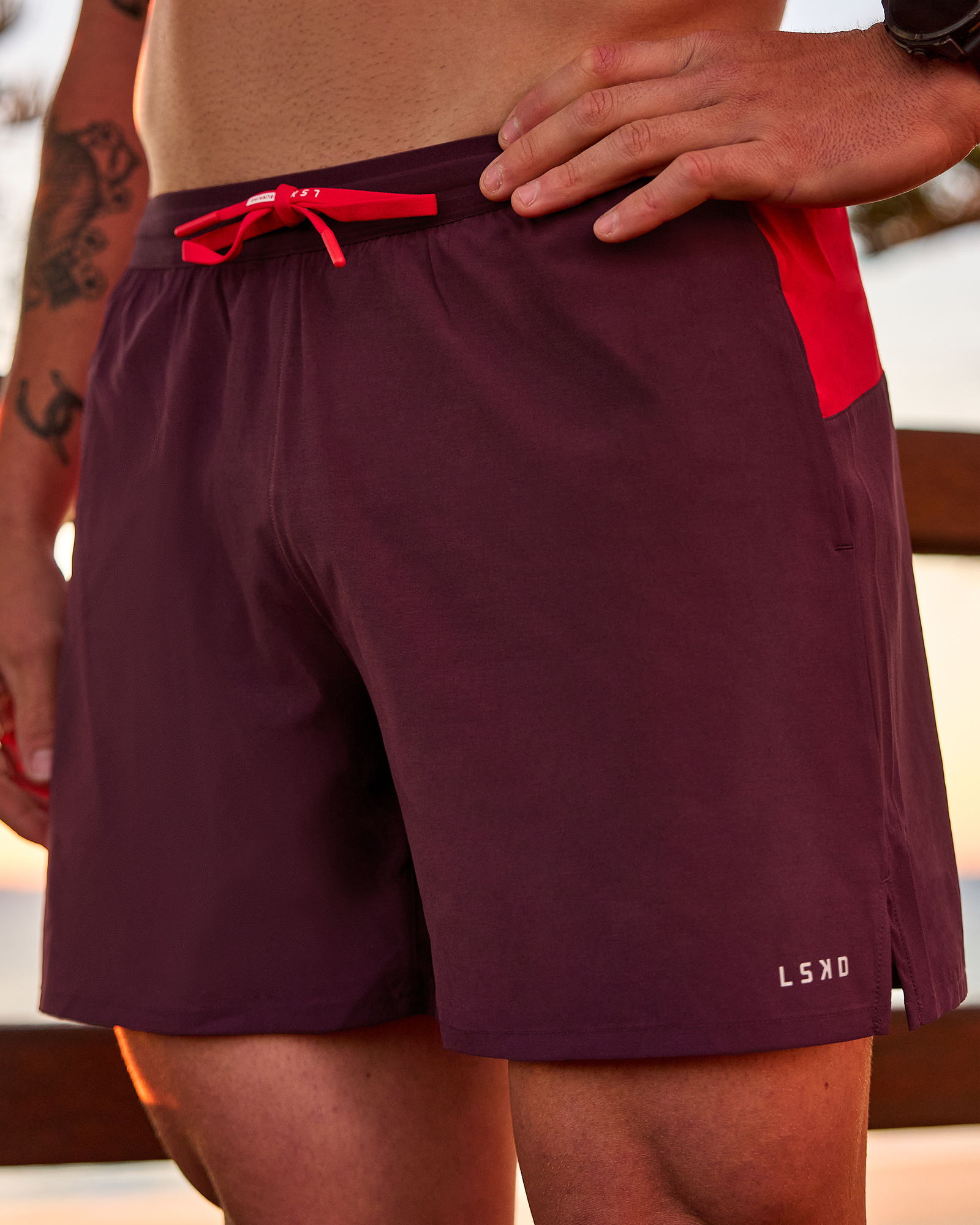 A person wearing maroon swim shorts with a red accent.