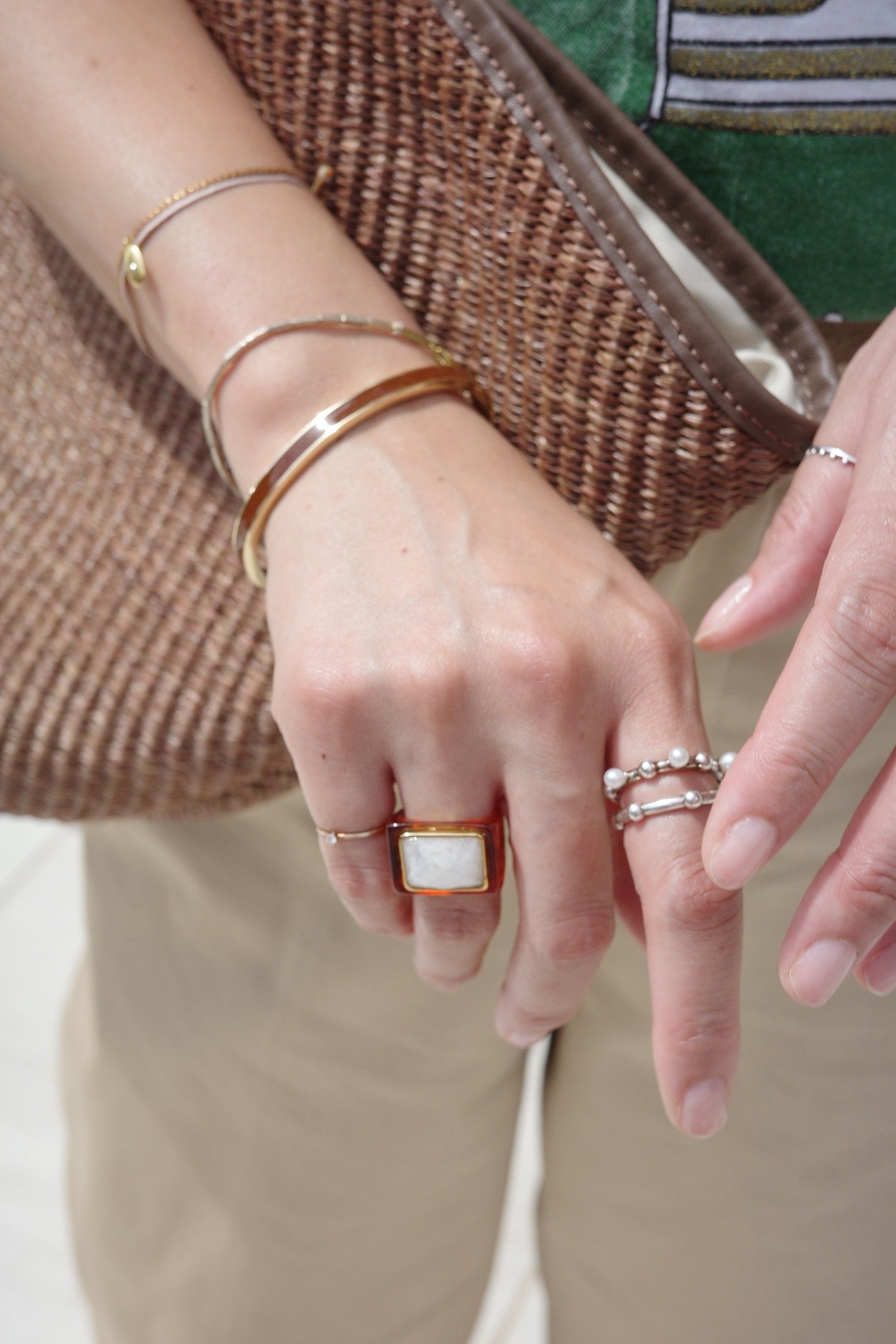 Close-up of hands wearing multiple rings and bracelets, with a bag in background.