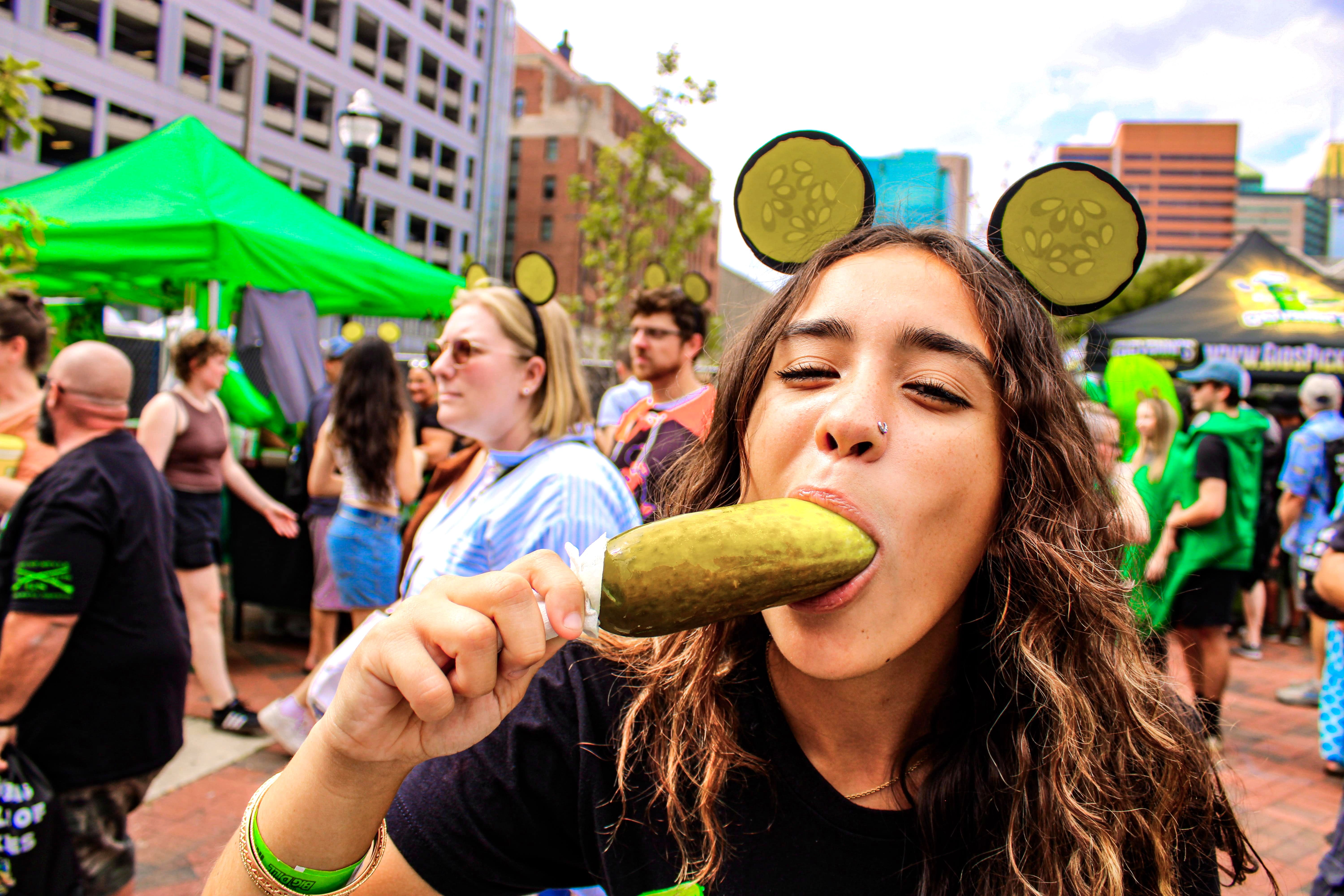 A pickle lover enjoys a giant dill pickle on a stick from Jersey Pickles at The Big Dill pickle festival, Power Plant Live!, Baltimore Maryland 2025