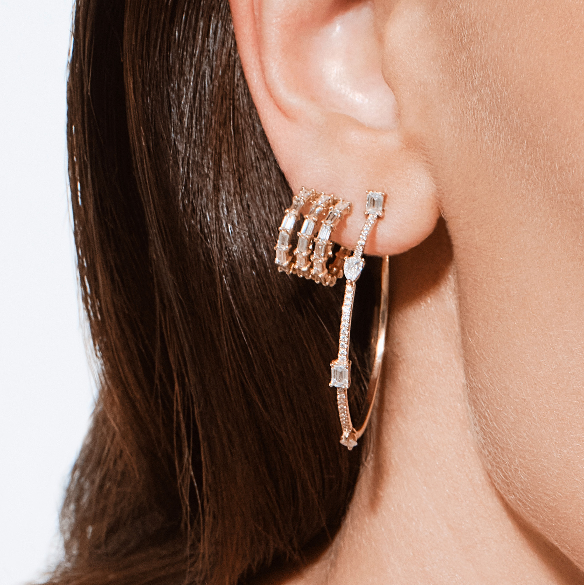 Close-up of a model wearing yellow gold pavé diamond hoop earrings layered with diamond ear cuffs and baguette diamond stud earrings.