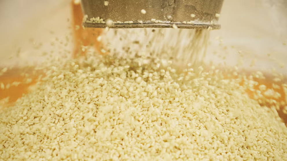 Grains pouring from a machine into a pile on a surface.