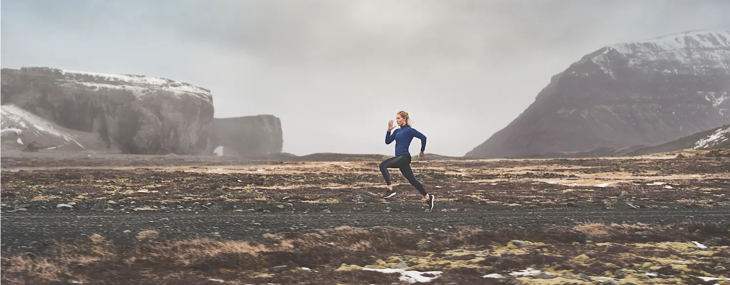 A woman running through rugged terrain with a garmin smartwatch