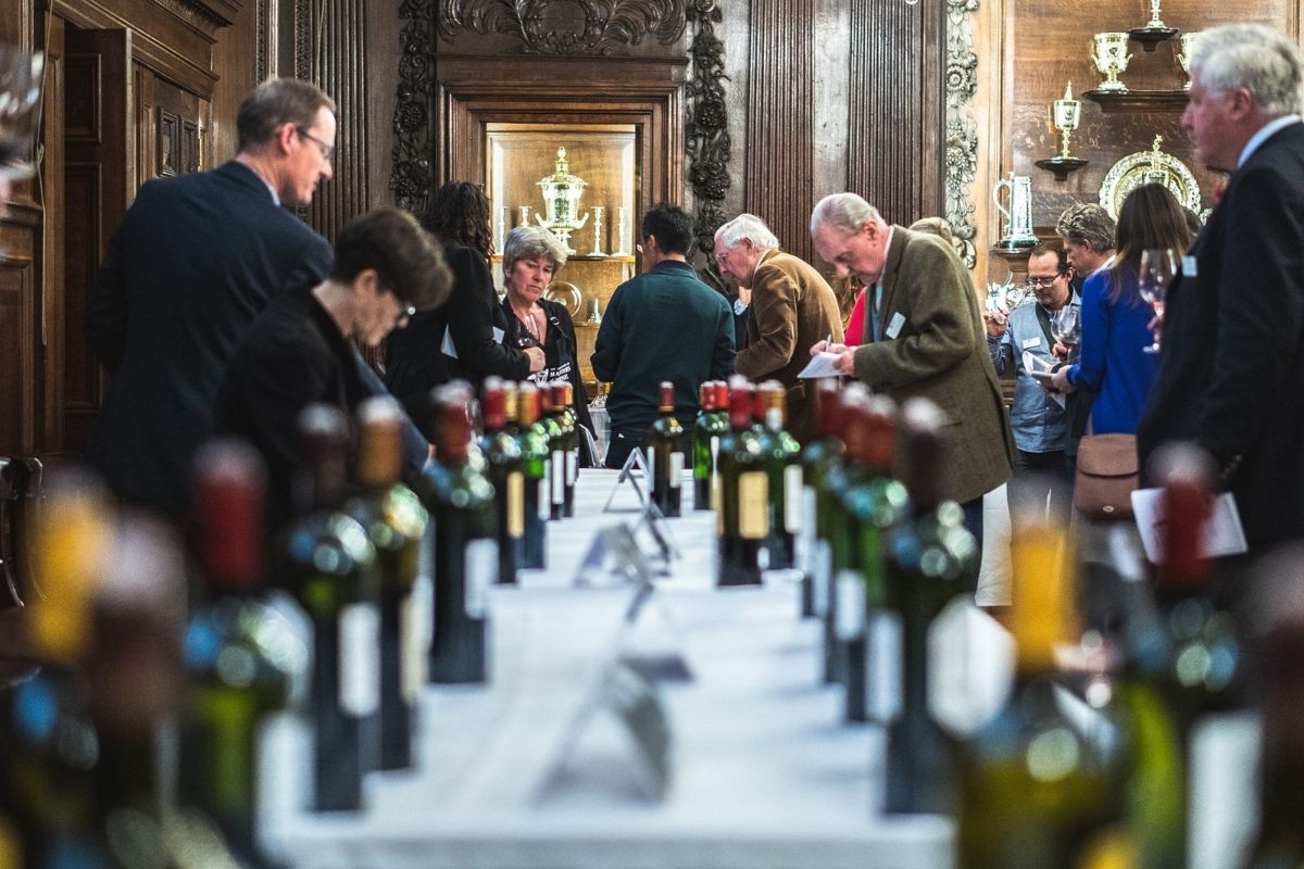 People tasting wine at an event with bottles lined on a table.