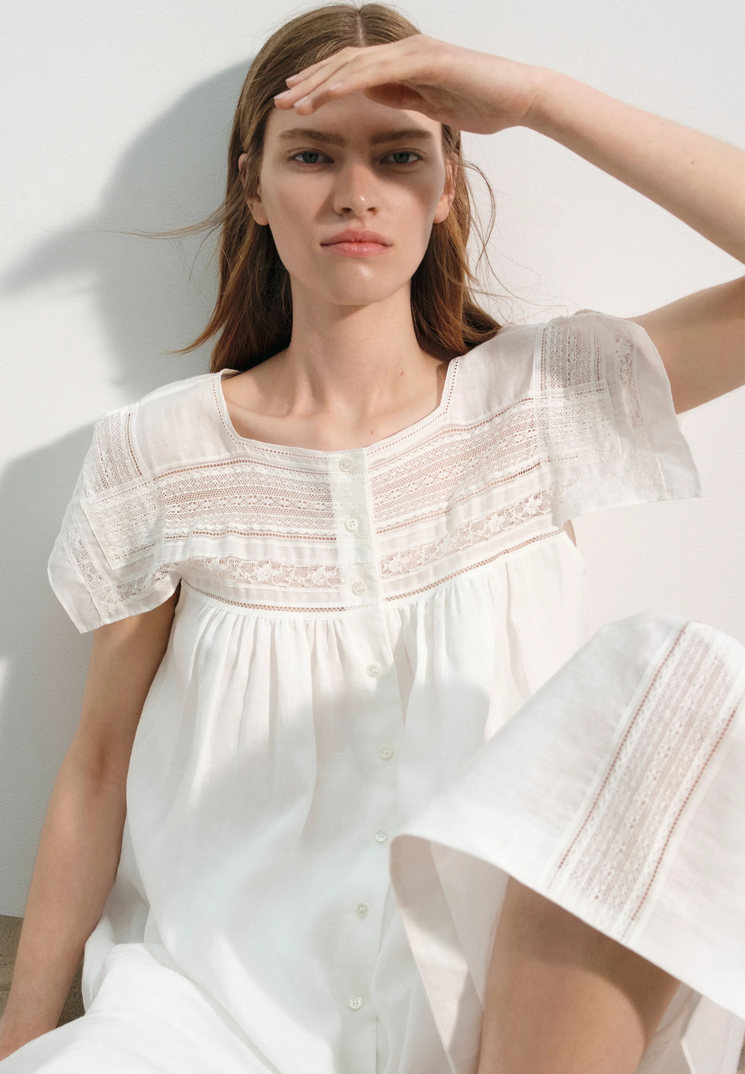 Model in a white dress, shielding eyes from sunlight.