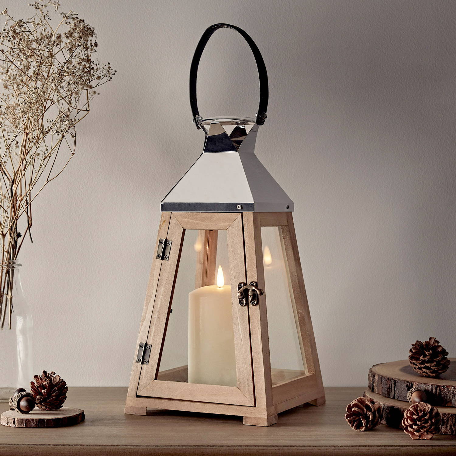 A wooden trapeze lantern with a candle inside on a shelf with acorns surrounding.